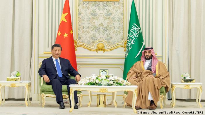 Saudi-Arabiens Kronprinz Mohammed bin Salman sitzt gemeinsam mit Xi Jinping vor einem mit Blumen gedeckten Tisch, im Hintergrund die Fahnen Chinas und Saudi-Arabiens