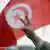 A hand displaying the peace sign in front of a Tunisian flag