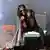 Steven Tyler tobt auf der Bühne und umfasst einen Mikrofonständer, der mit bunten Tüchern behangen ist.