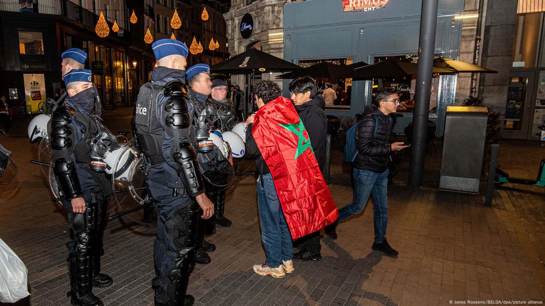 A group of Brussels police stop two young Morocco fans on the street as another youth walks past