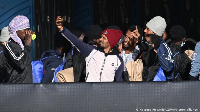Mit Taschen und Decken bepackte Bootsflüchtlinge posieren für ein Selfie