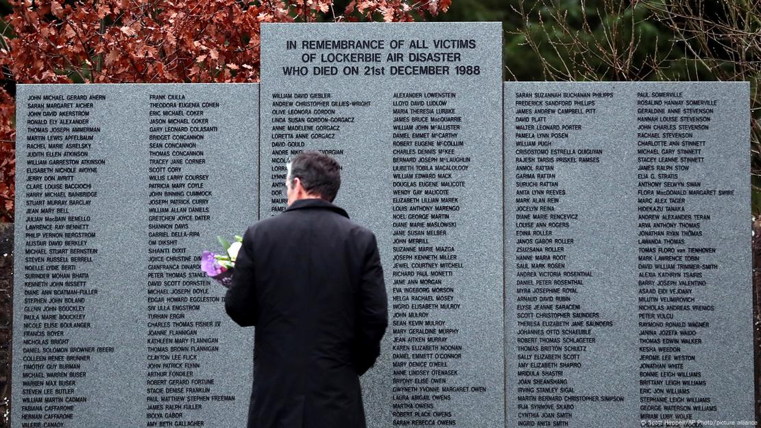 Homem em frente a memorial com lista de nomes