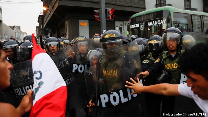 Manifestantes sostienen una bandera frente a un pelotón de policías antimotines