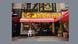A chef in white clothing sits in front of a deli with a bright yellow front. A chef in white clothing sits in front of a deli with a bright yellow front.