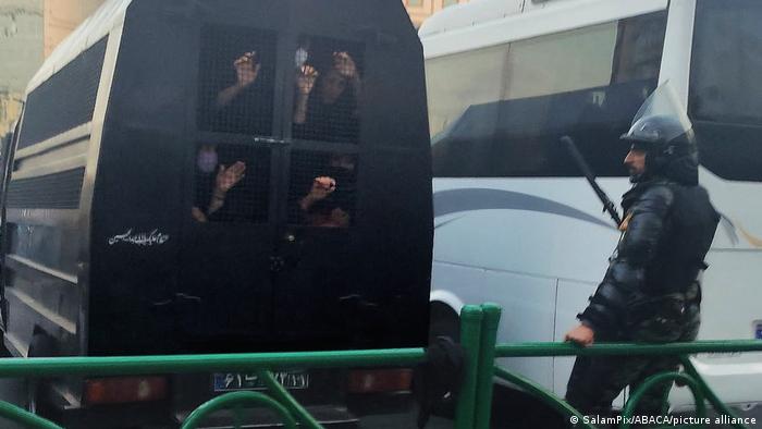 Policía observa cómo se aleja un grupo de personas detenidas en una furgoneta policial.