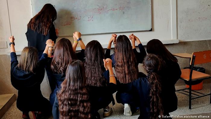 Protestierende iranische Schülerinnen ohne Kopftuch von hinten gesehen im Klassenzimmer