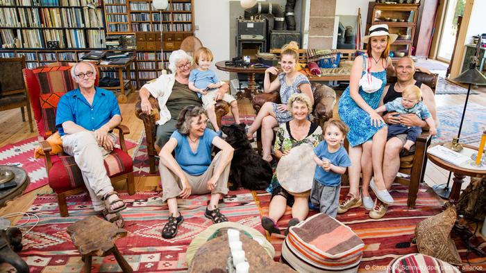Mehrgenerationen-Wohngemeinschaft in Deutschland. Junge und ältere Personen sitzen für das Gruppenfoto in einem Wohnraum. 