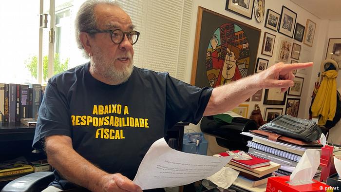 Der Schriftsteller Fernando Morais sitzt an seinem Schreibtisch mit einem Dokument in der Hand 