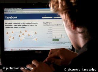 A young man sits in front of a computer with the Facebook website in shot