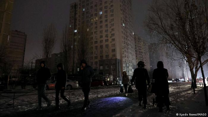 Menschen gehen in der Hauptstadt in Kiew durch dunkle Straßen, die nur von fahrenden Autos erleuchtet werden