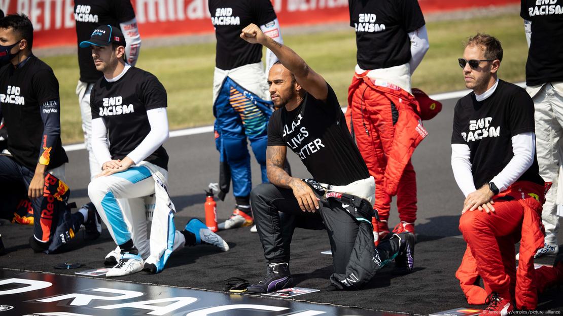 El piloto británico de F1 Lewis Hamilton y sus compañaeros de equipo se manifiestan con camisetas con letreros contra el racismo. Algunos tienen una rodilla sobre el terreno. Hamilton, además, levanta un puño.