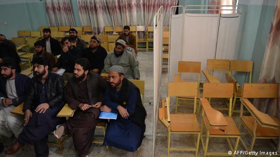 Male students are seen sitting in a classroom a university in Kandahar Province, Afghanistan, sitting next to a group of empty chairs hidden behind a white screen