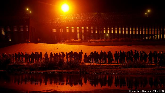 Una cantidad masiva de migrantes en busca de asilo, se paran cerca del muro fronterizo después de cruzar el río Bravo para entregarse a los agentes de la Patrulla Fronteriza de EE.UU. en El Paso, Texas.