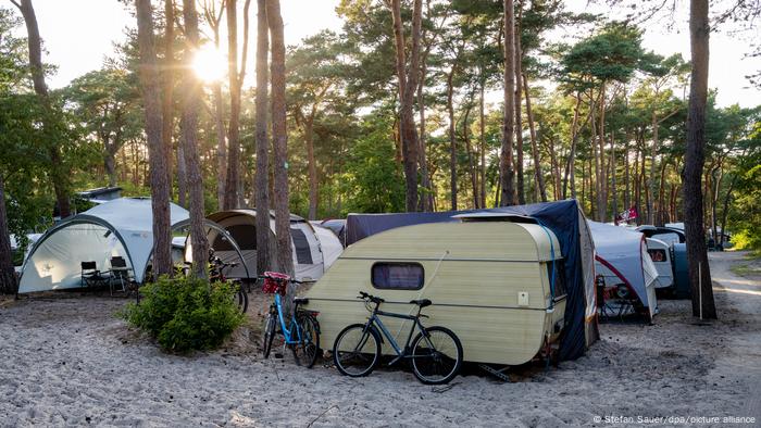 Wohnwagen stehen auf dem Campingplatz „Dünencamp“ auf der Insel Usedom im Sonnenuntergang unter Bäumen.