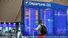 Eine Frau steht mit Ihrem Koffer vor der Departure/Abflug-Anzeige und schaut nach ihrem Flug.
