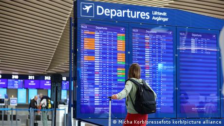 Eine Frau steht mit Ihrem Koffer vor der Departure/Abflug-Anzeige und schaut nach ihrem Flug.