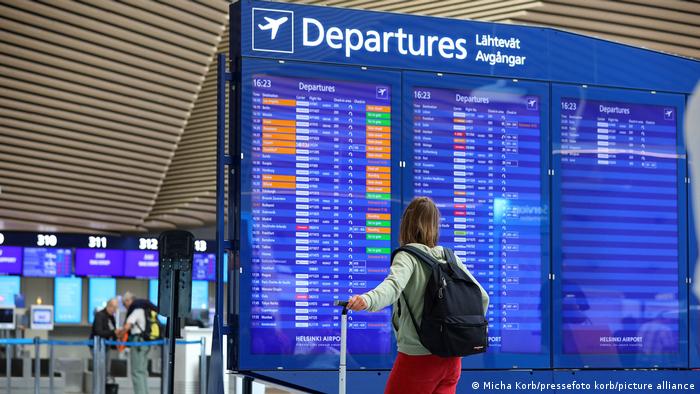 Eine Frau steht mit Ihrem Koffer vor der Departure/Abflug-Anzeige und schaut nach ihrem Flug.