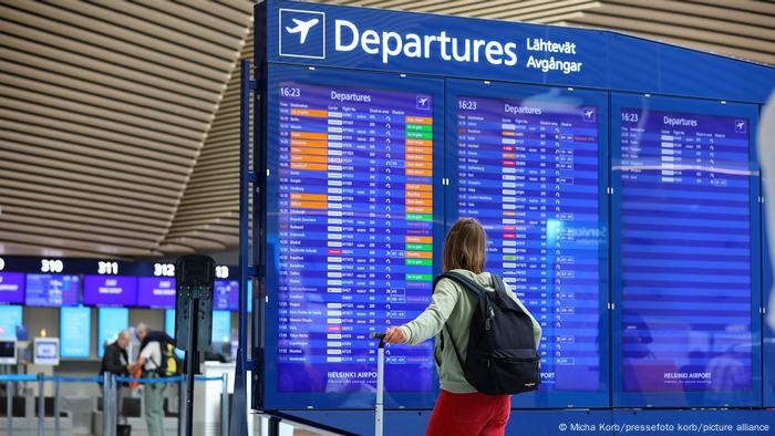 Eine Frau steht mit Ihrem Koffer vor der Departure/Abflug-Anzeige und schaut nach ihrem Flug. Eine Frau steht mit Ihrem Koffer vor der Departure/Abflug-Anzeige und schaut nach ihrem Flug.