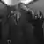 Schwarz-weiß Foto aus dem Film Oppenheimer: Ein Mann fasst sich an den Hut auf seinem Kopf, er ist umringt von Menschen mit Fotokameras