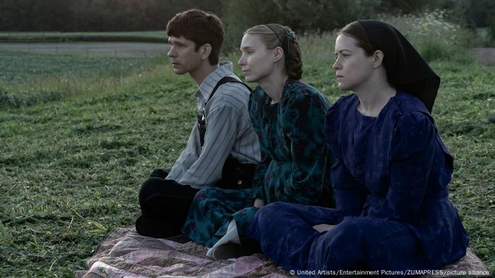Filmszene: Ein Mann und zwei Frauen sitzen auf einer Decke in der Natur