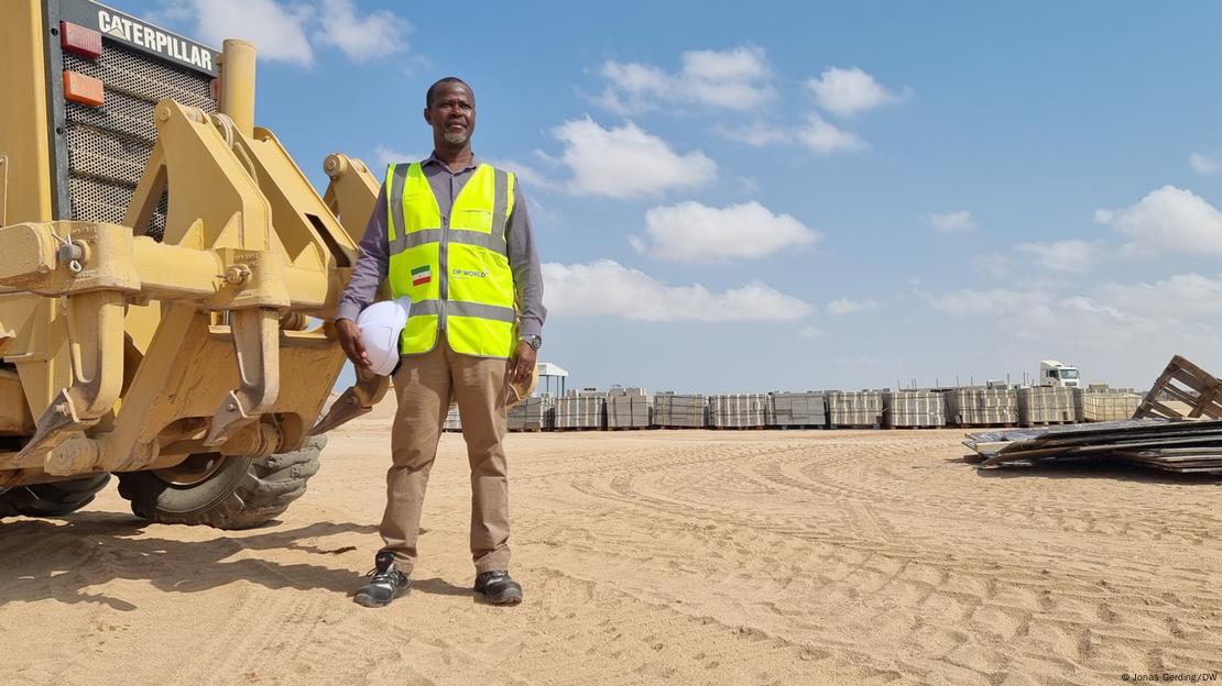A picture of Joseph Oguta standing helmet in hand next to a bulldozer