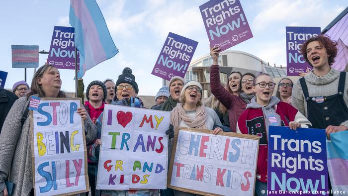 Vor dem schottischen Parlament stehen Menschen mit bunten Plakaten, auf denen mehr Rechte für Trans-Menschen und andere Solidaritäts-Botschaften stehen