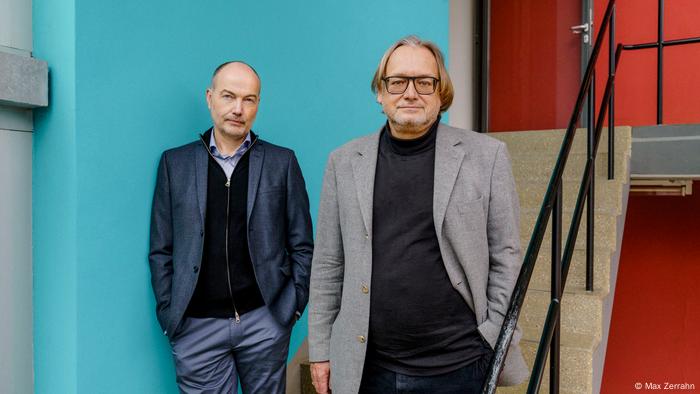 Kai Michel und Harald Meller stehen vor zwei bunten Wänden und einer Treppe