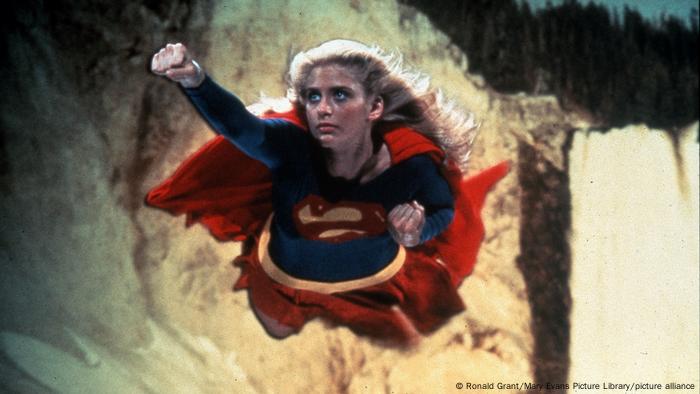 Eine blonde Frau fliegt im Supermankostüm durch die Luft.