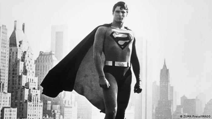Ein Mensch im Supermankostüm steht vor einer Skyline.