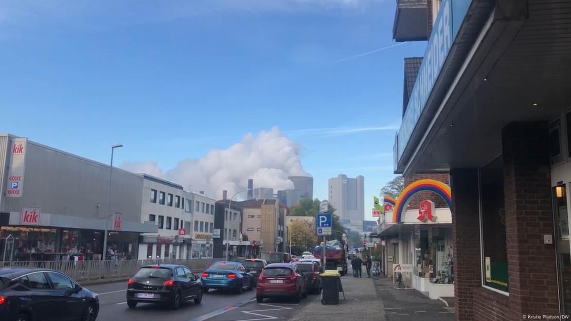 Coluna de fumaça de uma usina é vista ao final de uma rua cheia de carros.