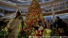 Visitors, some wearing face masks, gather to take souvenir pictures with a giant Christmas tree decorated at a hotel on the eve of Christmas in Beijing, Saturday, Dec. 24, 2022. (AP Photo/Andy Wong)