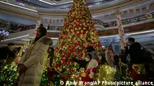 Visitors, some wearing face masks, gather to take souvenir pictures with a giant Christmas tree decorated at a hotel on the eve of Christmas in Beijing, Saturday, Dec. 24, 2022. (AP Photo/Andy Wong)