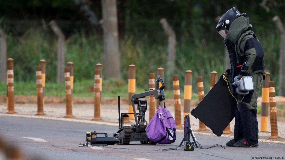 Homem com roupa especial de proteo desativa bomba em uma mochila roxa