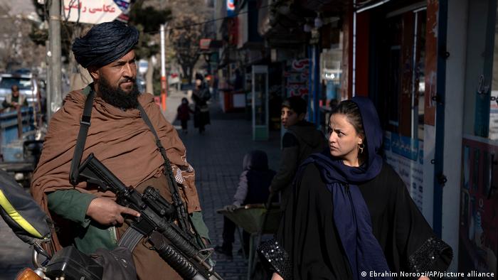 Un talibán con un rife se acerca a una mujer que camina por la calle en Kabul.