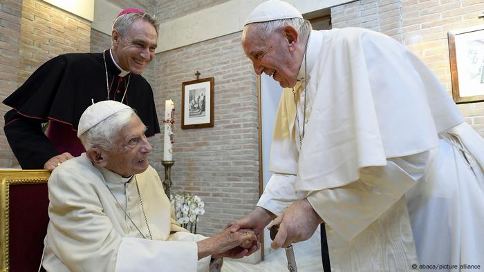 Papst Franziskus gibt dem emeritierten Papst Benedikt XVI. (sitzend) die Hand