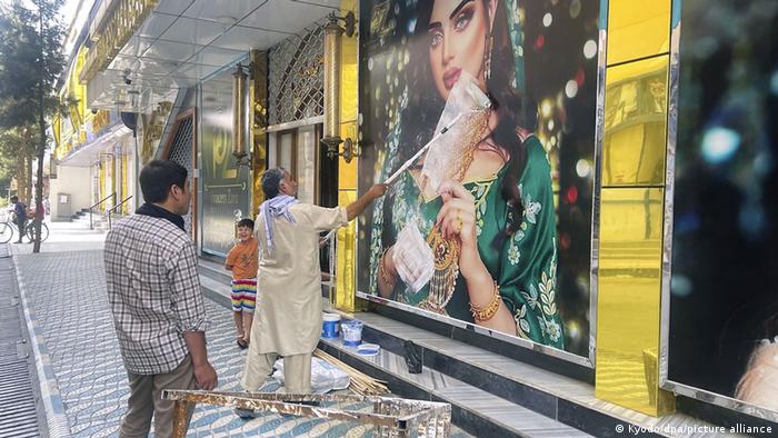 Un hombre pinta con un rodillo sobre la imagen de una mujer en el escaparate de una tienda de moda.