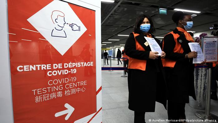 Flughafenmitarbeiterinnen warten auf Passagiere aus China vor einem Coronavirus-Testbereich am Pariser Flughafen Charles de Gaulle