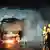 Nachtaufnahme: Ein Bus brennt, vorne rechts sind Feuerwehrleute mit Helmen zu sehen