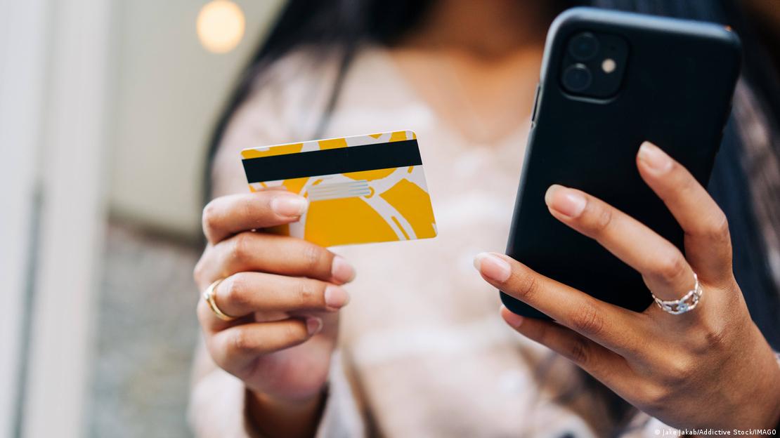 Bir elinde cep telefonu, diğer elinde banka kartıyla internetten alışveriş yapan bir kadın.