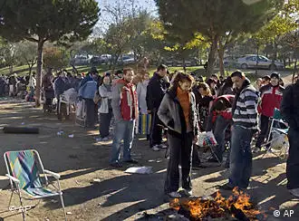 People warm up near a fire as they wait in line to buy a cheap apartment in Fuenlabrada, on the outskirts of Madrid, on Saturday, Nov. 15, 2008. Over 2,300 people have been taking turns to sleep outside, in tents, to register for a future property development by Spanish developer Jose Moreno. Moreno, who has built other unusually low cost projects before, has promised to build 2,100 cheap apartments for young people who don't own any property yet. With over 2.8 million unemployed people and a slowing economy, Spain is suffering badly from the bursting of a housing bubble with sales falling 40 percent. (AP Photo/Daniel Ochoa de Olza)