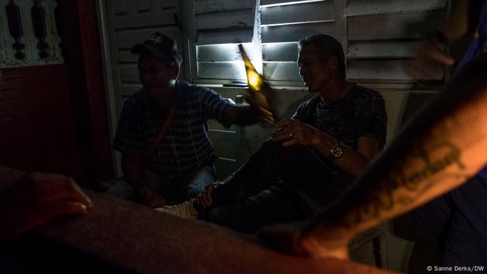 Unos hombres comparten una botella de ron en la terraza mientras esperan a que vuelva la luz.