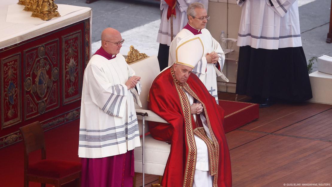 Papa Francisco sentado em uma cadeira, com dois homens de batina de cada lado