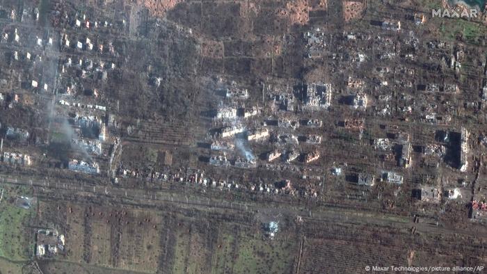 Imagen de satélite en color que muestra edificios destruidos en medio del campo, tomada directamente desde arriba.