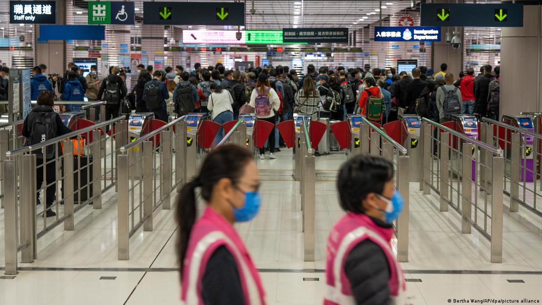 在香港落马洲车站的离境大厅，旅客们正在等待前往中国大陆的边境口岸重新开放。一名戴着口罩的工作人员从他们身旁走过
