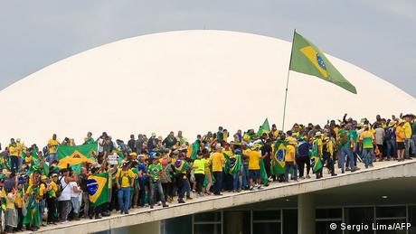 Decenas de personas con banderas de Brasil caminan por parte del techo del Congreso en Brasilia.