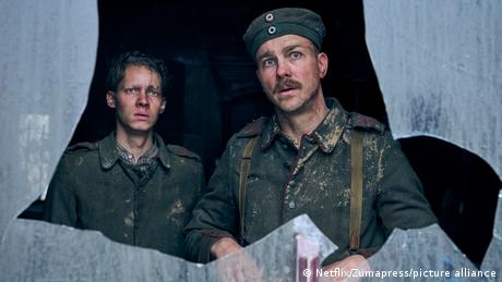 Filmszene aus Im Westen nichts Neues zeigt zwei junge, geschockte deutsche Soldaten, hinter zerbrochenem Glas
