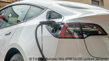 Schleswig, ein weißer Tesla Model 3, mit einem eingesteckten Ladestecker, parkt zum Aufladen auf einem E-Parkplatz. +++ Nur für redaktionelle Nutzung +++ Only for editorial use +++