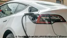 Schleswig, ein weißer Tesla Model 3, mit einem eingesteckten Ladestecker, parkt zum Aufladen auf einem E-Parkplatz. +++ Nur für redaktionelle Nutzung +++ Only for editorial use +++