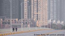 FILE - In this Jan. 28, 2020 file photo, people wearing face masks walk down a deserted street in Wuhan in central China's Hubei Province. Arek and Jenina Rataj were starting a new life in the Chinese industrial center of Wuhan when a viral outbreak spread across the city of 11 million. While they were relatively safe sheltering at home, Arek felt compelled to go out and document the outbreak of the new type of coronavirus. Among his subjects: the construction of a new hospital built in a handful of days; biosecurity check points; and empty streets. (AP Photo/Arek Rataj, File)