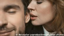 Woman kisses or whispers in man's ear. Selective focus on female lips near male ear in the center of image. Passionate couple in love. Close up shot.